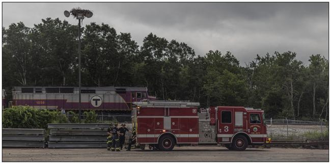 Fire truck and crew at a safety drill, in front of a Commuter Rail train.